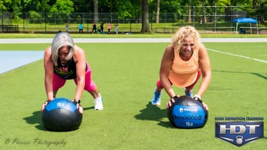 Two women exercising with medicine balls on a field