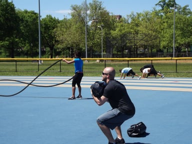 People exercising outdoors in a park with battle ropes and weights.