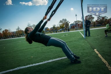 Woman performing TRX training outdoors on a field.