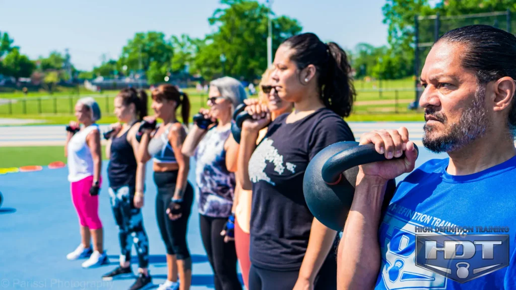 Adults performing kettlebell exercises together during an outdoor group fitness class